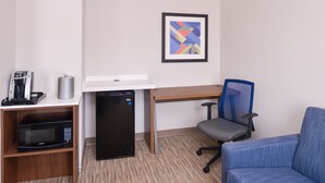 Habitación de hotel con escritorio, silla, microondas, refrigerador pequeño y cafetera.