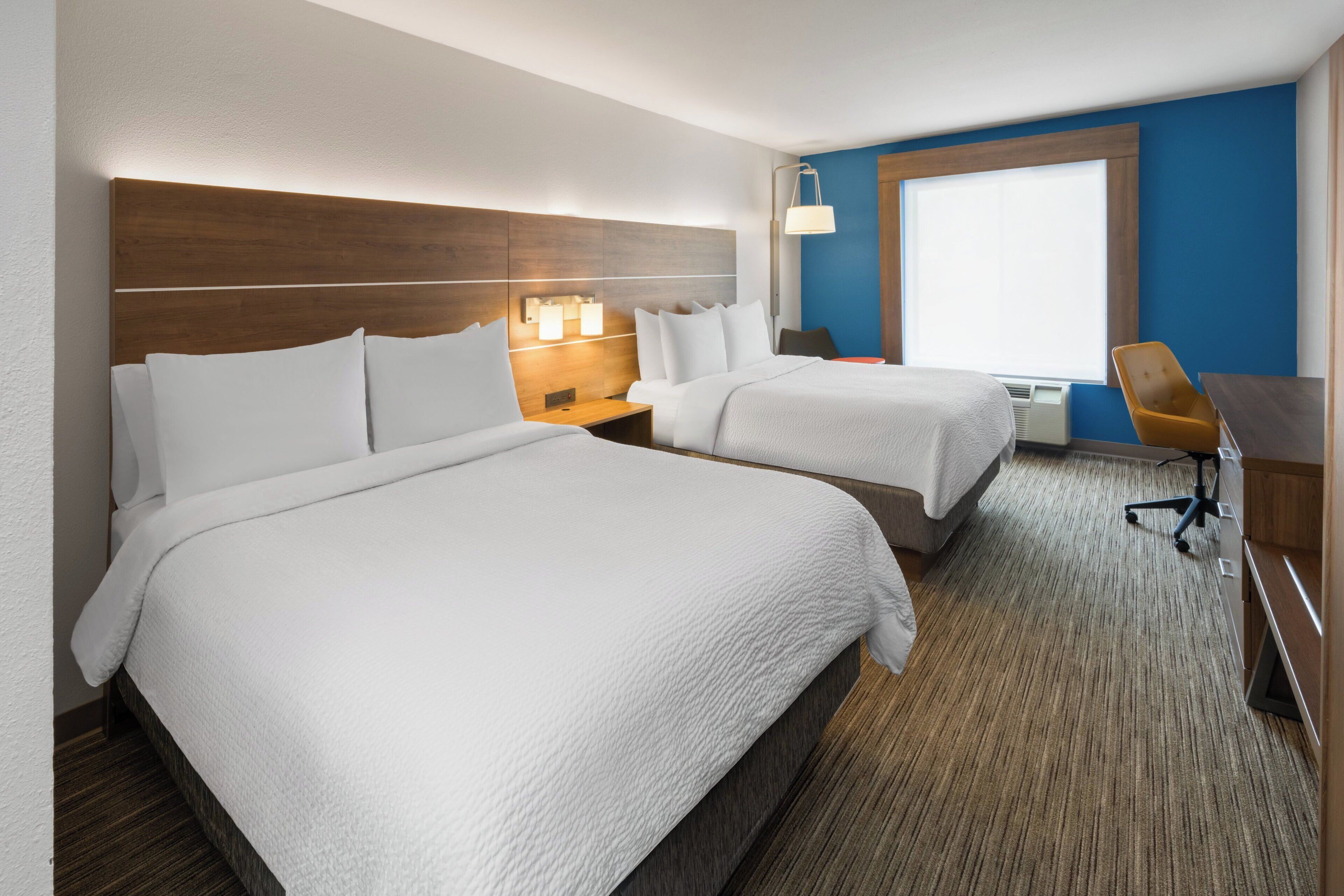 Quarto de hotel com duas camas, uma escrivaninha, uma cadeira e uma janela.