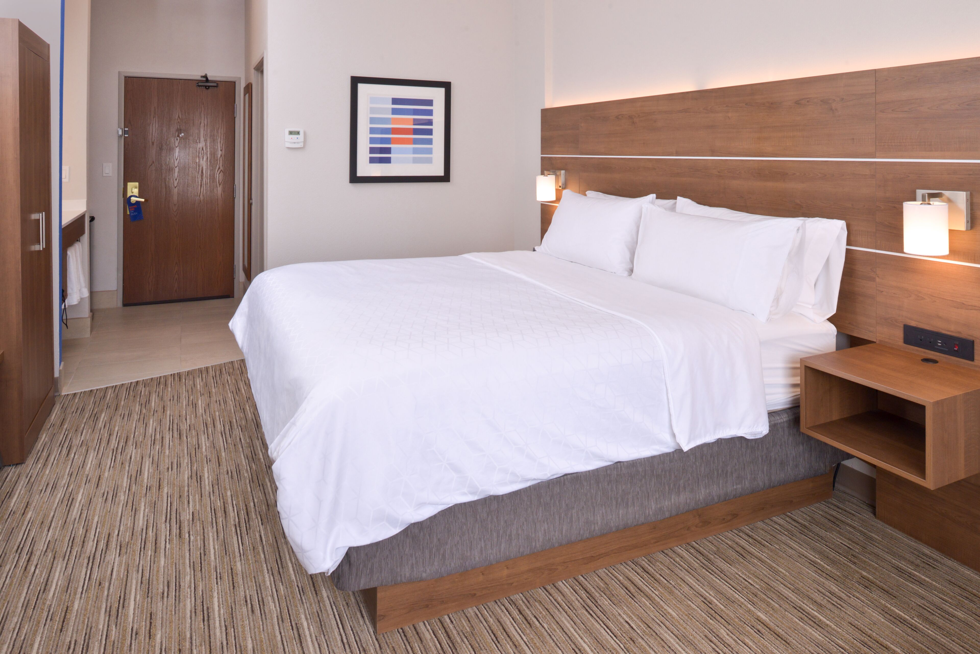 A hotel room with a large bed, wooden headboard, bedside tables, and a framed picture on the wall.