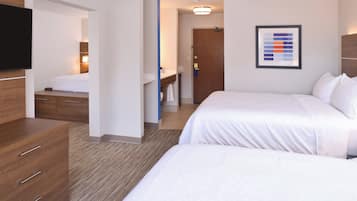 Una habitación de hotel con cama, tocador, televisor y baño visible a través de una puerta abierta.