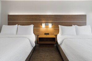 Habitación de hotel con dos camas, cabecera de madera, lámparas de noche y mesitas.