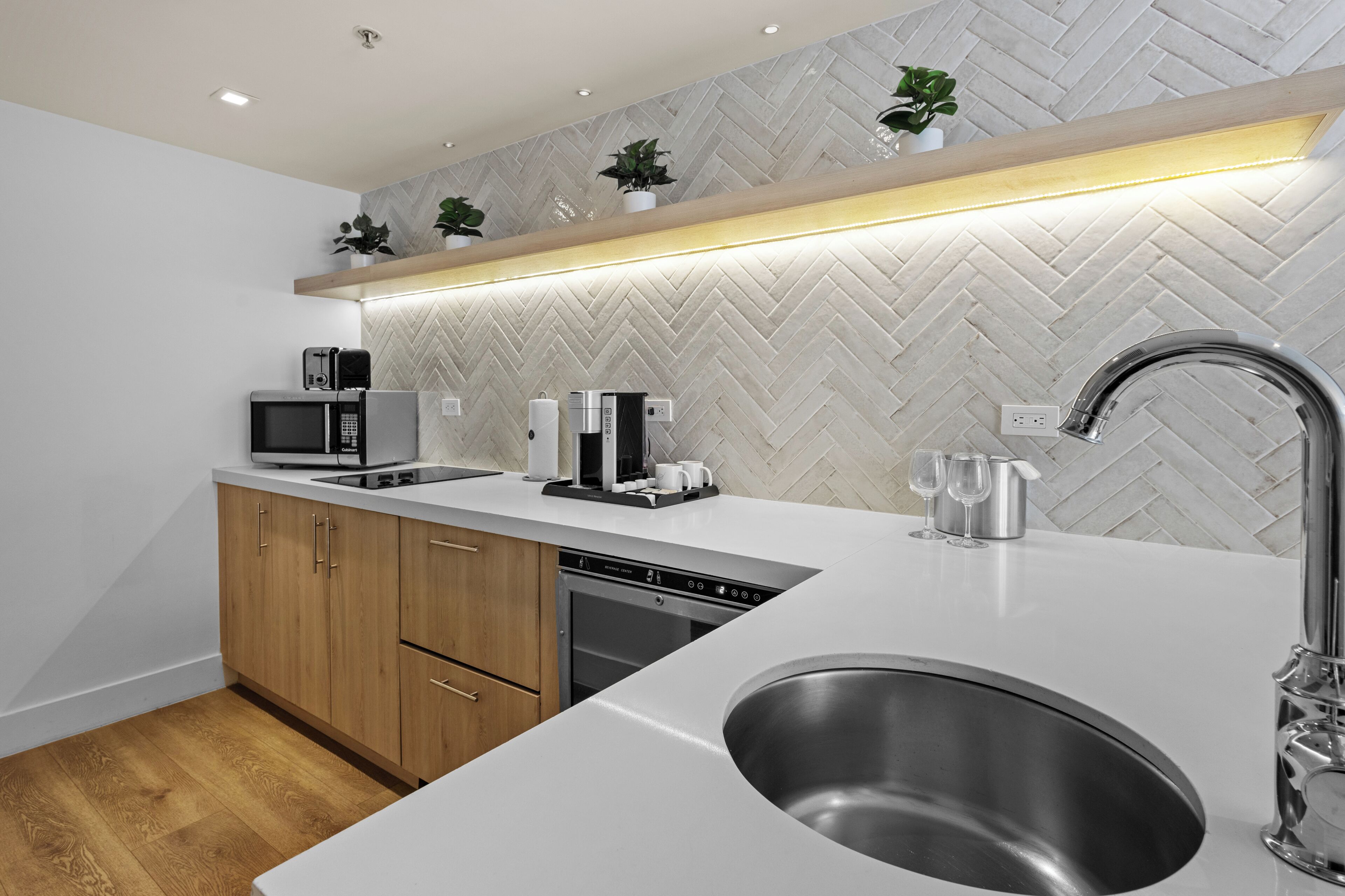 Cozinha moderna com backsplash de azulejos em padrão herringbone, eletrodomésticos de aço inoxidável e armários de madeira.