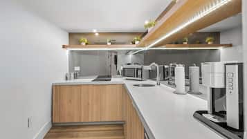 A modern kitchen with a white countertop, wooden cabinets, a built-in microwave, a coffee machine, and a small island with a sink.