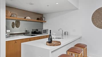 A modern kitchen with white countertops, wooden cabinets, a built-in microwave, and a wine bottle on the island.