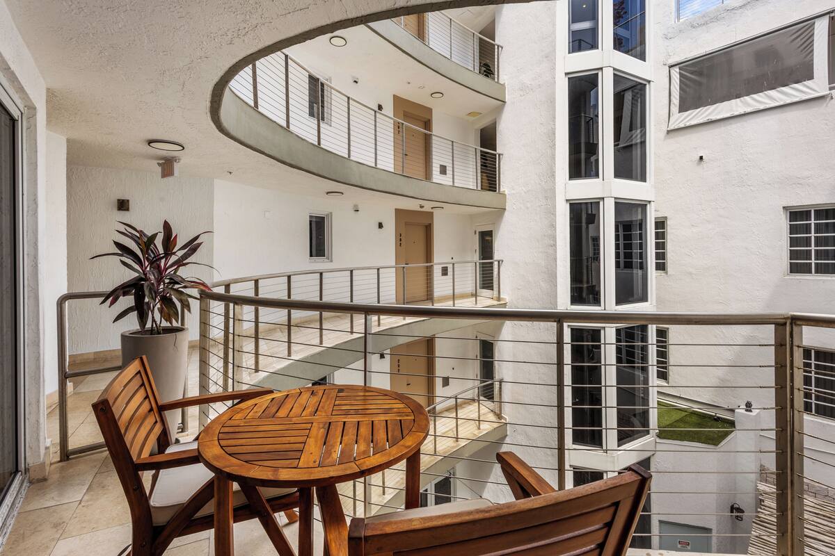 Un immeuble résidentiel à plusieurs étages doté d’un balcon, de meubles en bois et d’une plante en pot.