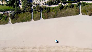 Oversigtsbillede af en strand med en enkelt strandstol, krystalklart turkis vand og en tæt skovlinje i baggrunden.