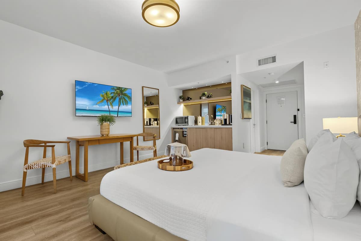 Une chambre d’hôtel comprenant un lit, un bureau, une chaise, une télévision, un coin cuisine et une porte.