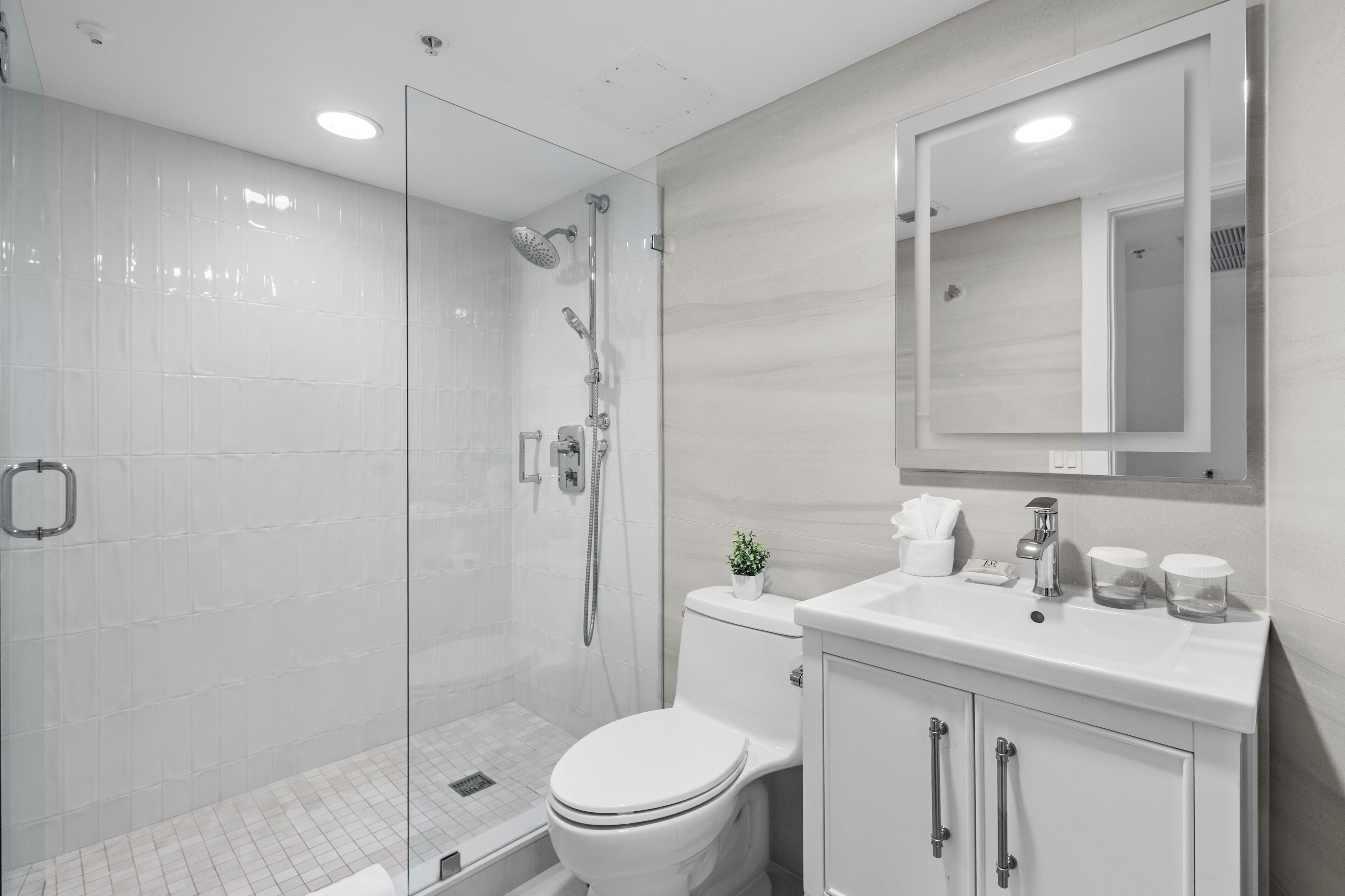 Une salle de bain moderne avec une douche à parois de verre, des toilettes blanches et un meuble-lavabo avec un miroir.