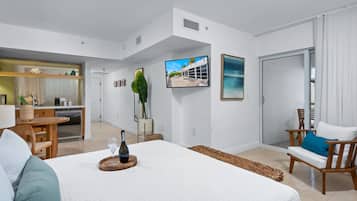 A spacious room with a large bed, a dining area, a kitchen, and a TV mounted on the wall.