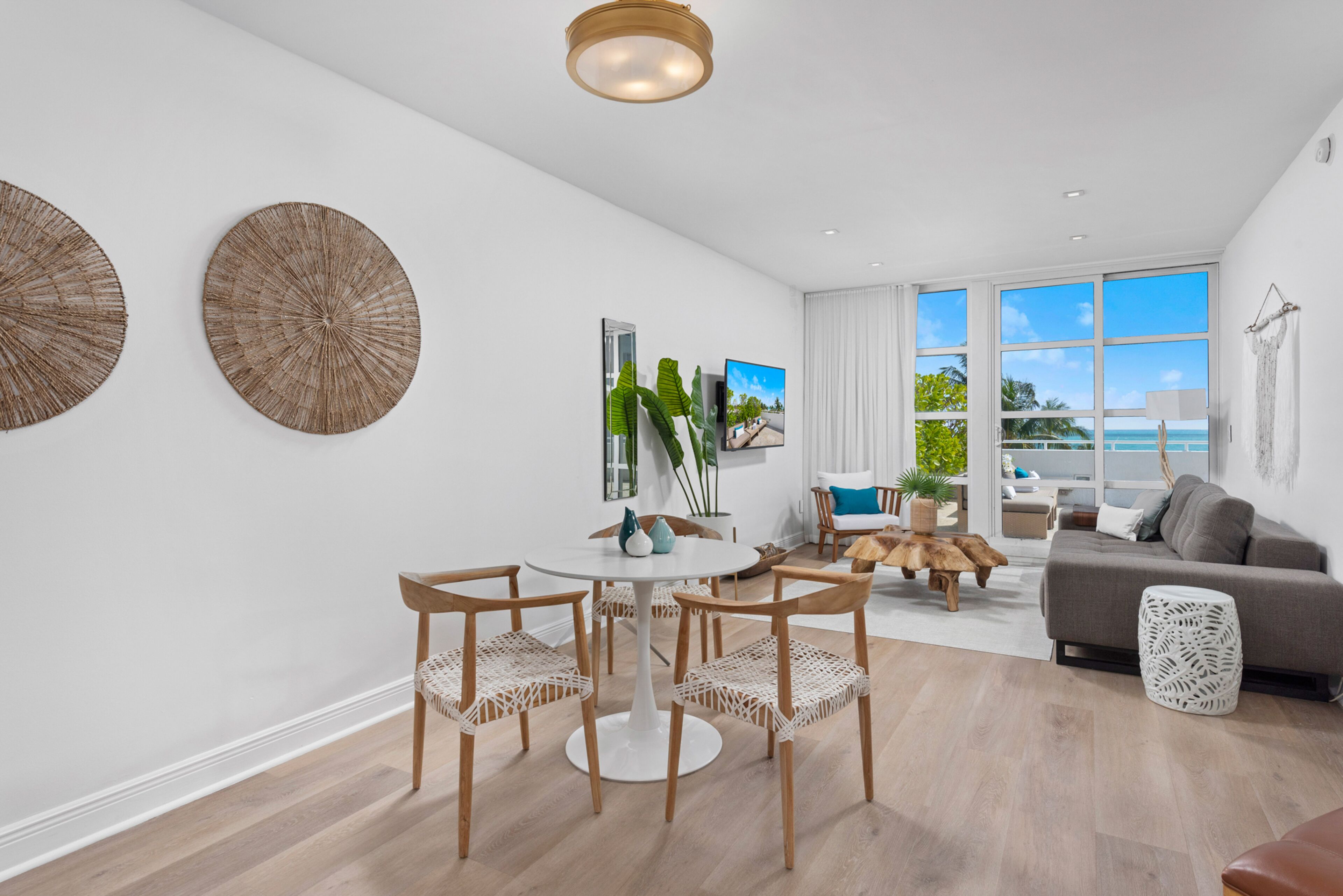 A modern living room with a round table, four chairs, a sofa, and a large window offering a view of the ocean.