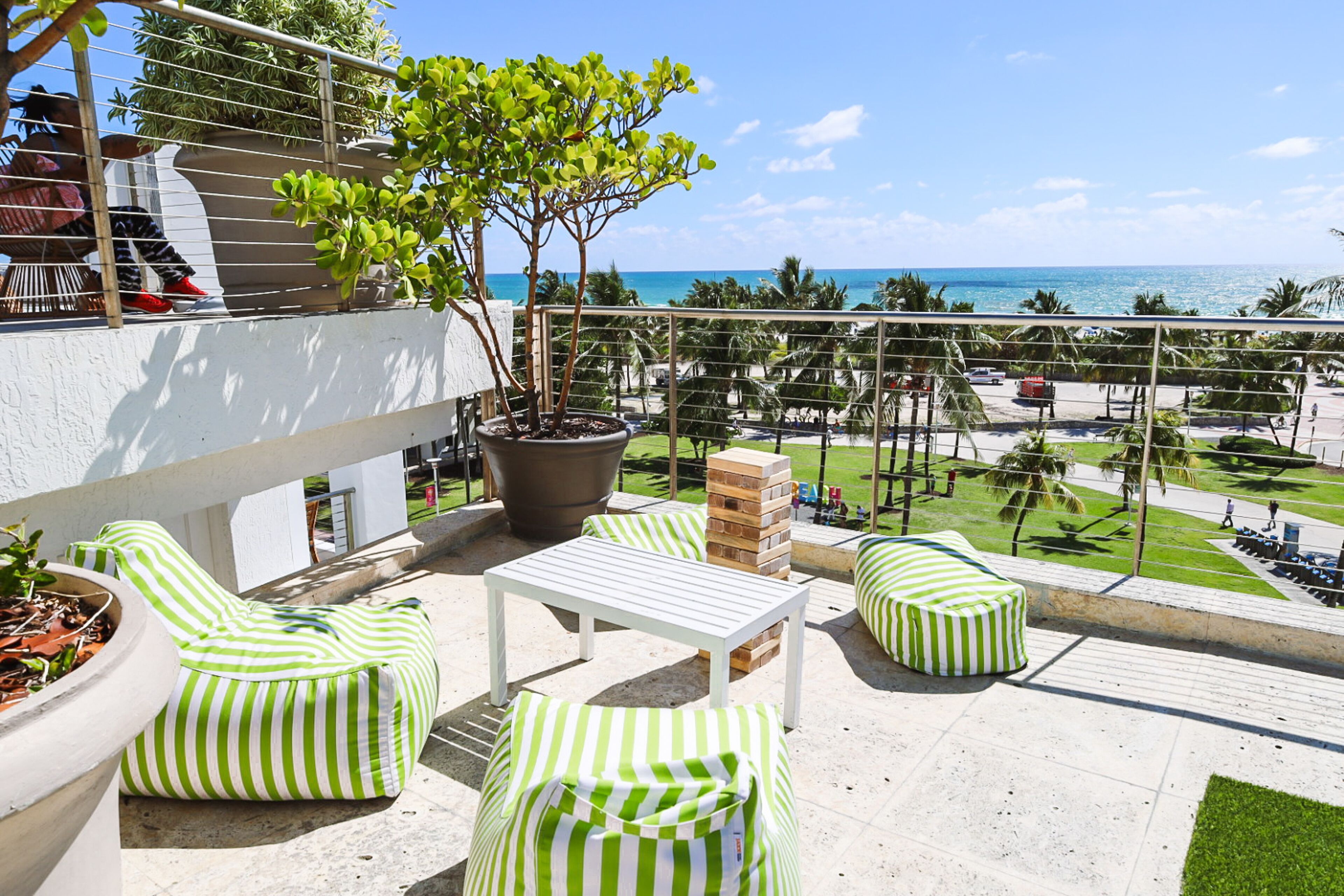 A balcony with green-striped seating, a potted tree, and a view of the beach.