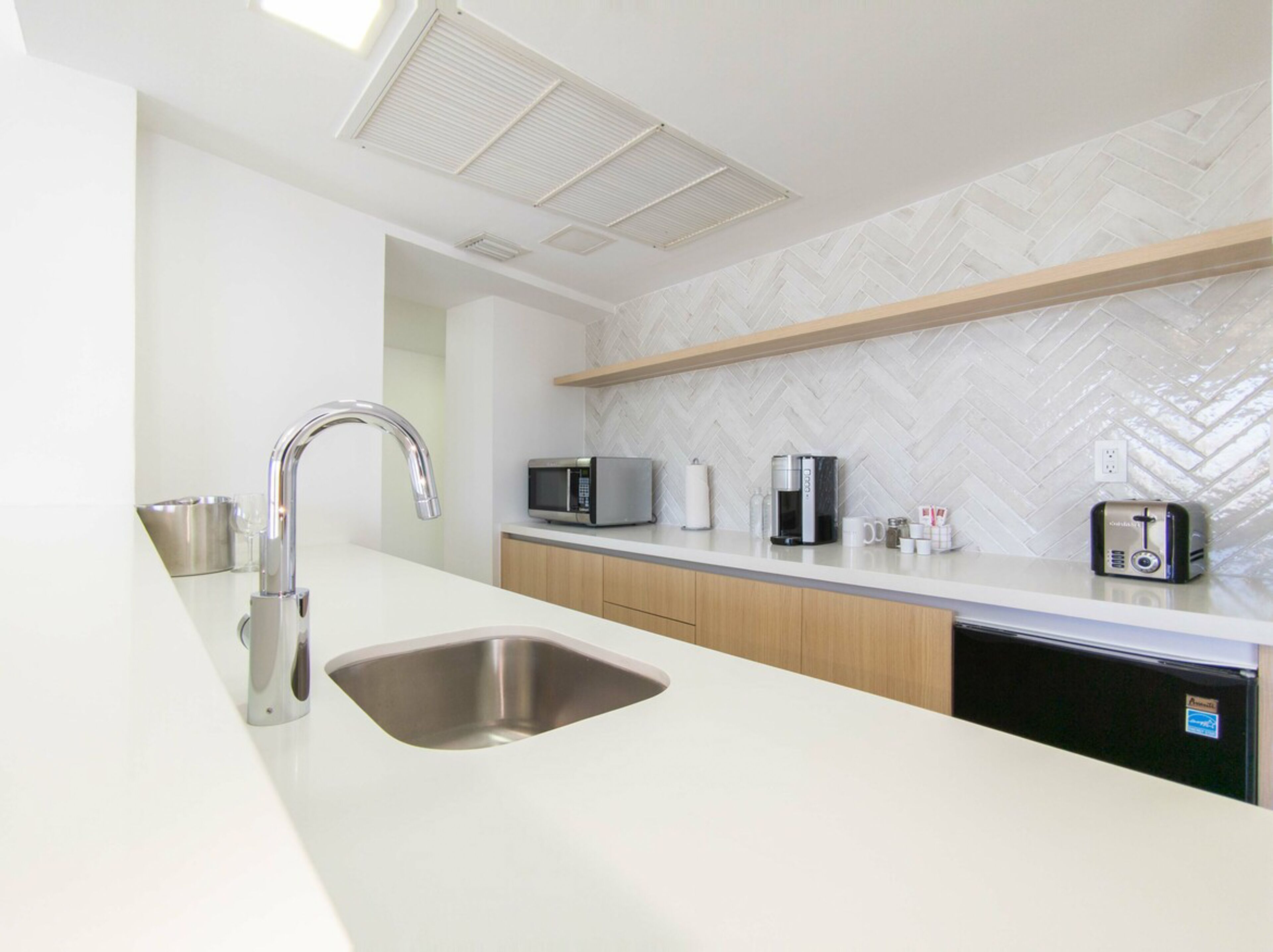 A modern kitchen with a stainless steel sink, a microwave, a coffee maker, and a toaster on the countertop.