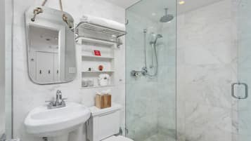 A modern bathroom with a glass-enclosed shower, a white sink, and a mirror with a rope handle.