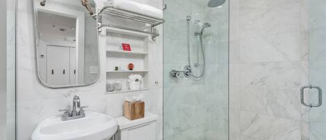 A modern bathroom with a glass-enclosed shower, a white sink, and a mirror with a rope handle.