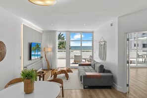 A modern living room with a sofa, dining table, and a view of the beach.