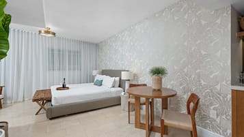 A modern hotel room with a bed, a dining table, chairs, a lamp, and a potted plant.