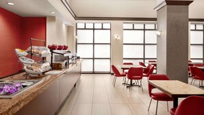 A modern dining area with a buffet counter, red chairs, and large windows. - Ramada by Wyndham Suites Orlando Airport (Orlando)