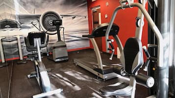 A gym with cardio machines, weight benches, and a wall mural of a car and clouds.