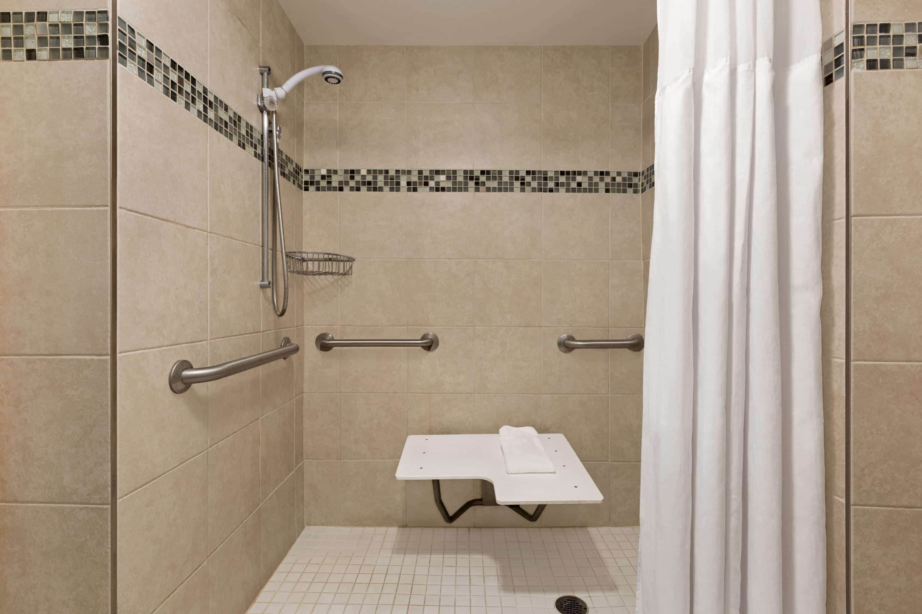 A shower with a grab bar, a towel rack, and a tiled floor.