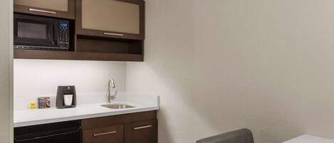 Una kitchenette compacta con microondas, cafetera y pileta. Hay dos sillas y una mesita.