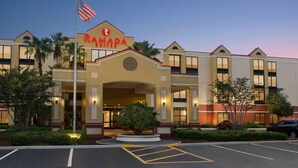A Ramada hotel with a prominent entrance, flag, and well-lit facade. - Ramada by Wyndham Suites Orlando Airport (Orlando)