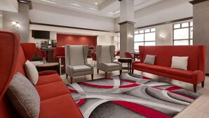 A modern lobby with a red sofa, grey armchairs, and a patterned rug. - Ramada by Wyndham Suites Orlando Airport (Orlando)