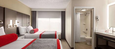A hotel room with two beds, a bathroom, and a shower area.