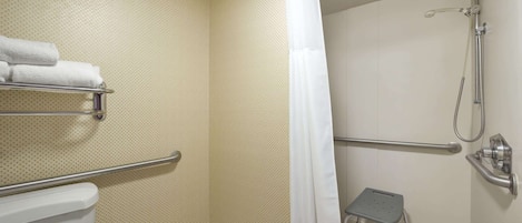 Un baño con inodoro, ducha con barra de apoyo, taburete y toallero.