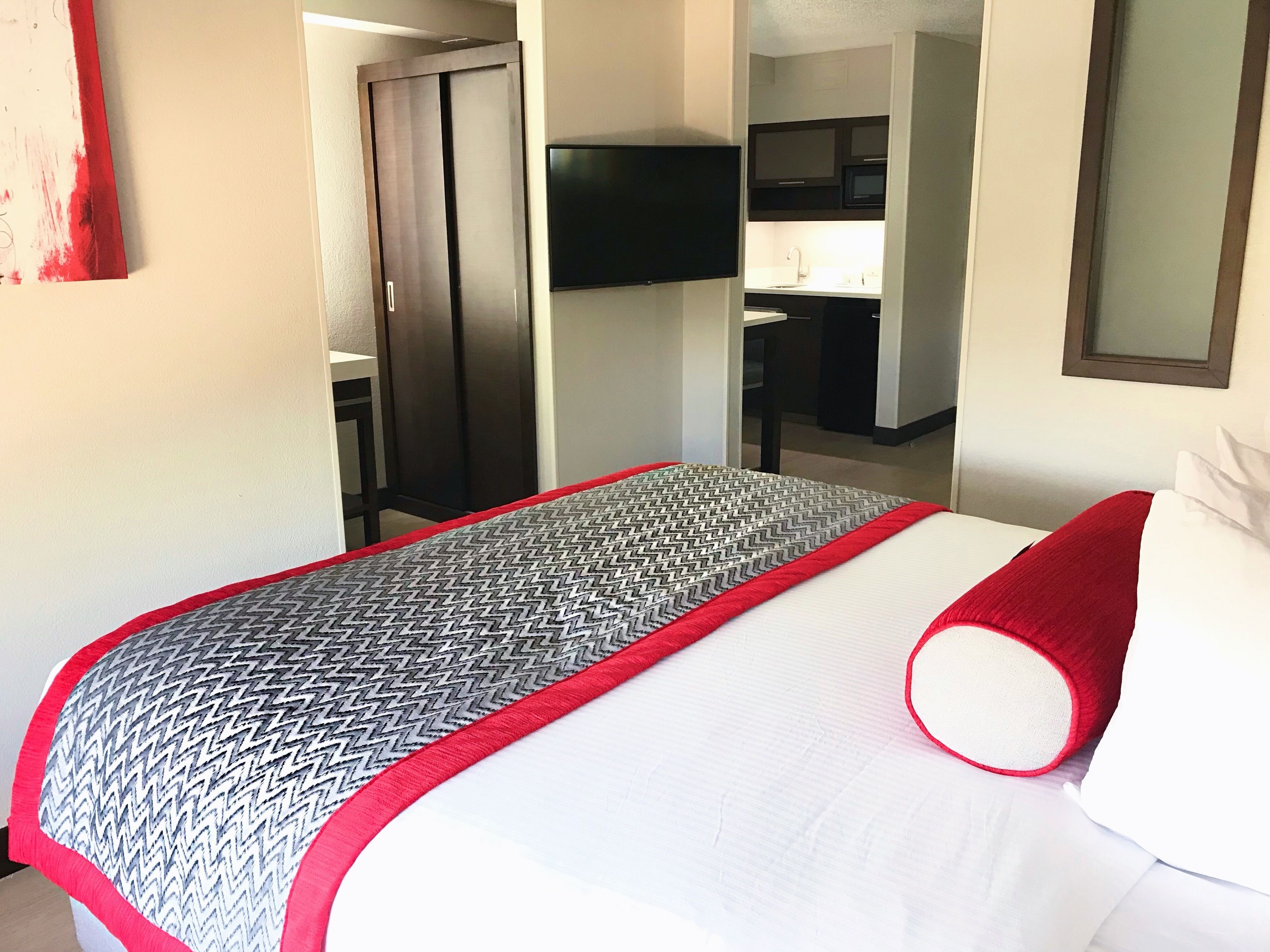 A hotel room with a bed, a television mounted on the wall, and a wardrobe.