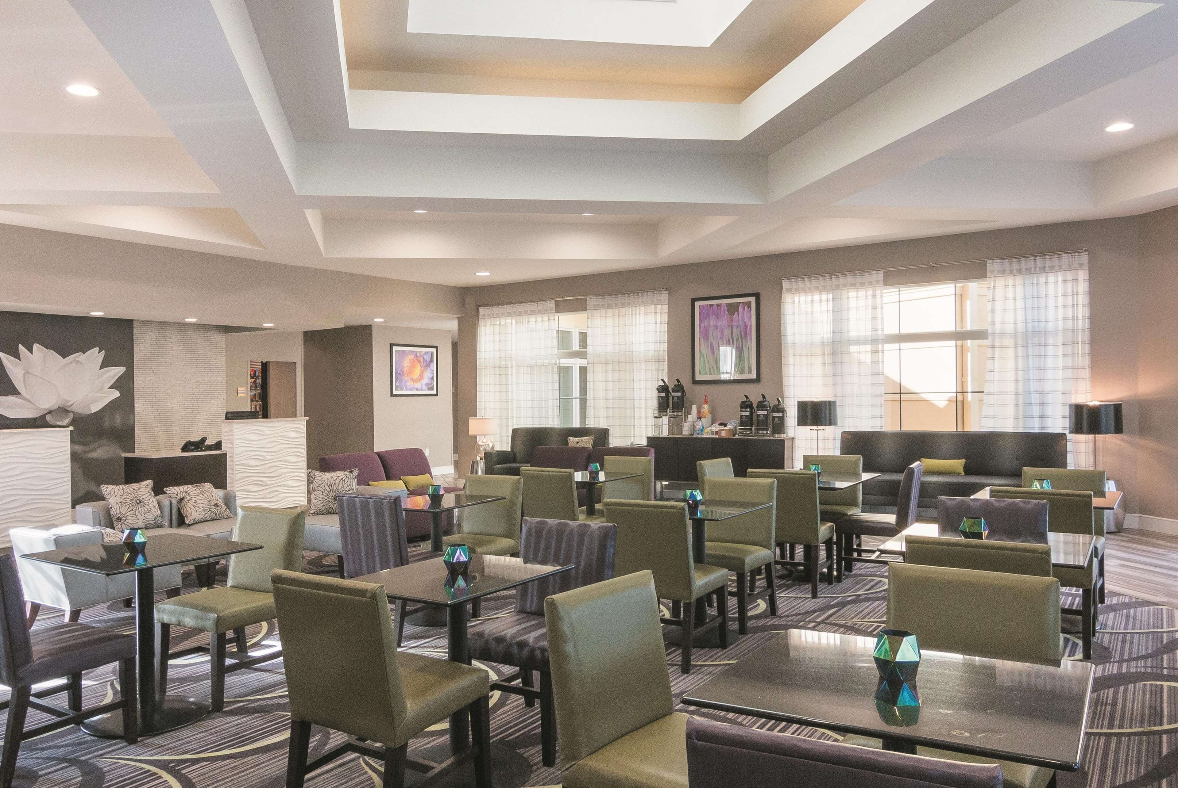 Un hall de hotel con varias zonas de estar, incluyendo sofás y sillones, dispuestos alrededor de mesas. Hay ventanas amplias con cortinas, un mostrador de recepción y obras de arte en las paredes.