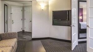 A hotel room with a sofa, a television mounted on the wall, and a door leading to another room. - La Quinta Inn & Suites by Wyndham Orlando Airport (Orlando)