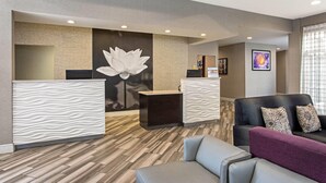 A reception area with a modern design, featuring a reception desk, a large floral wall art, and a seating area with a sofa and armchairs. - La Quinta Inn & Suites by Wyndham Orlando Airport (Orlando)