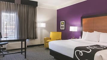 A hotel room with a bed, a desk, a chair, a lamp, and a window with curtains.