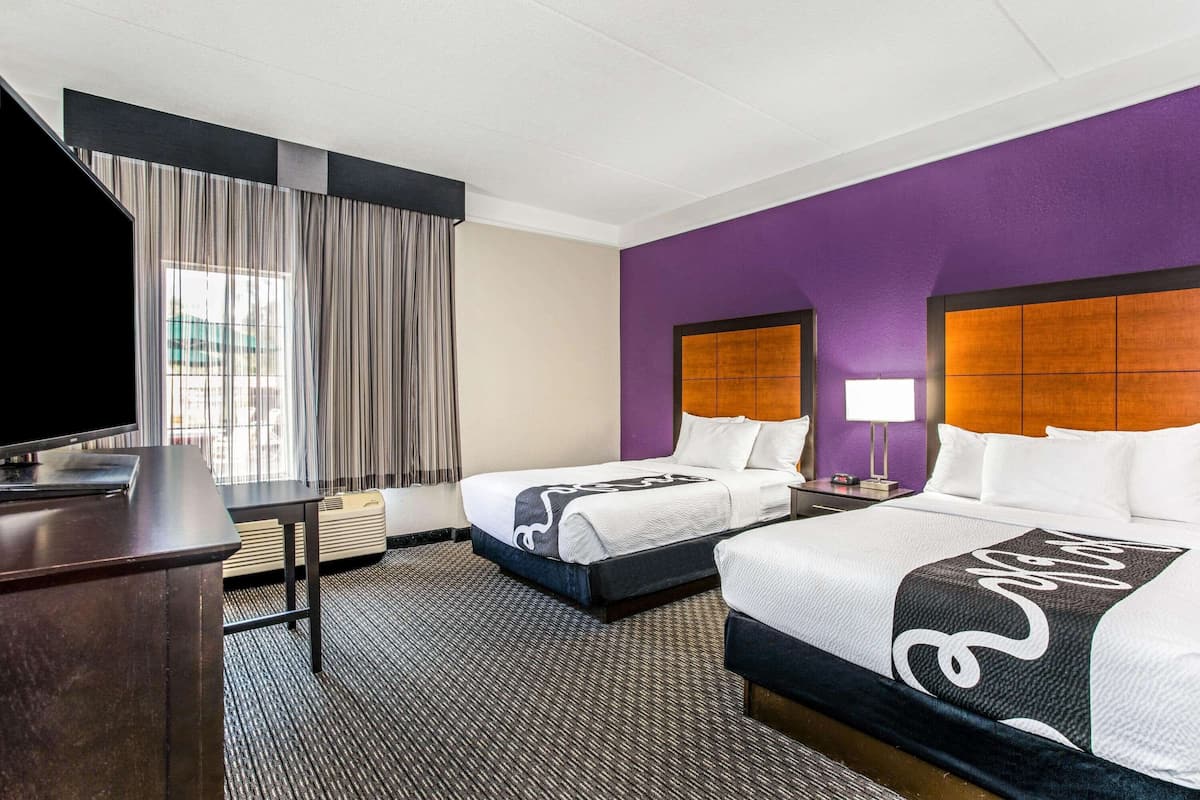 Ett hotellrum med två sängar, en TV, ett skrivbord och ett fönster med gardiner.
