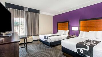 A hotel room with two beds, a TV, a desk, and a window with curtains.