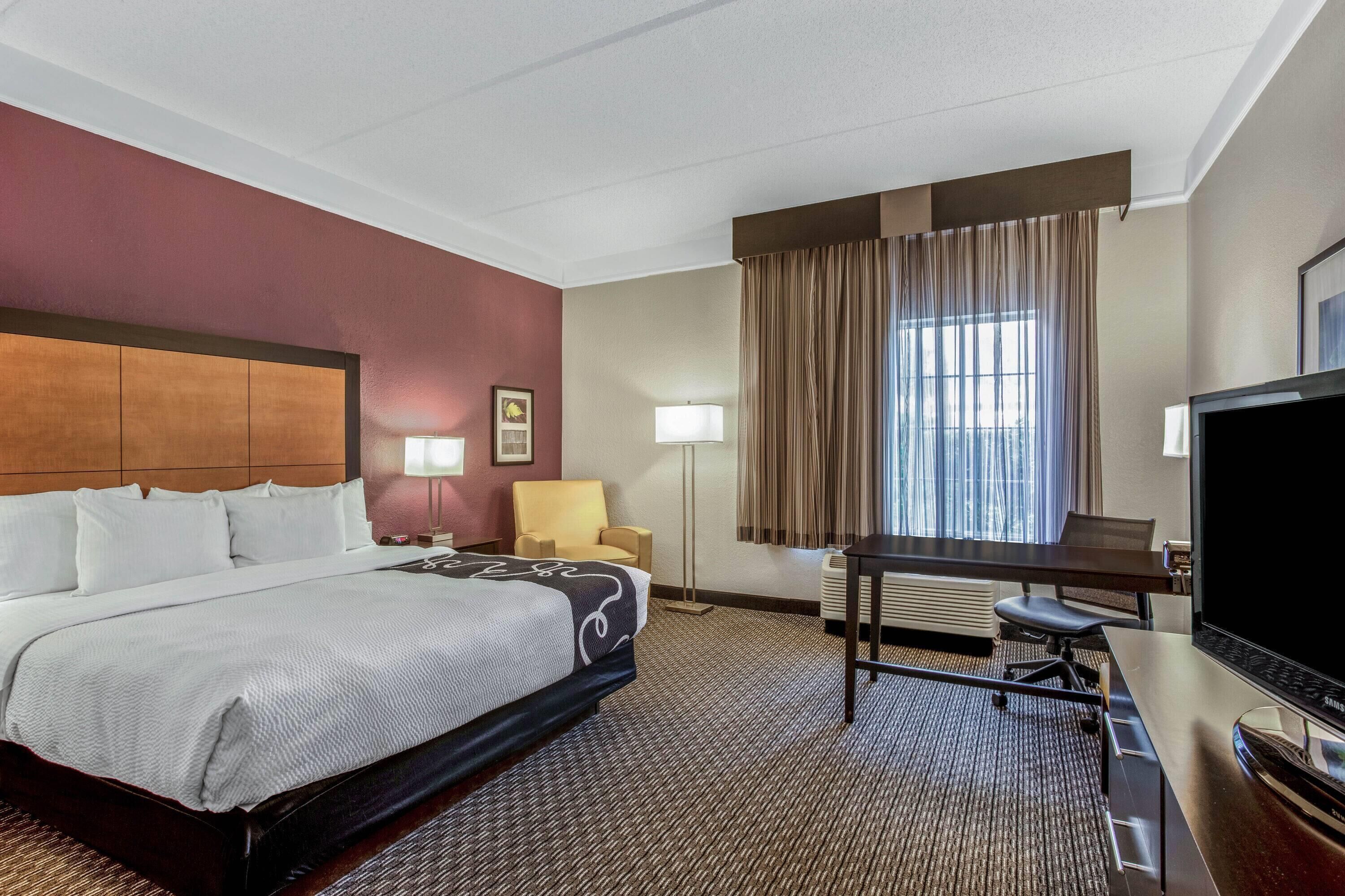 Une chambre d’hôtel avec un grand lit, un bureau avec un ordinateur, une télévision et une fenêtre avec des rideaux.
