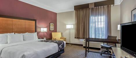 A hotel room with a large bed, a desk with a computer, a television, and a window with curtains.