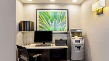 A corner room with a desk, computer, printer, lamp, chair, and an ATM.