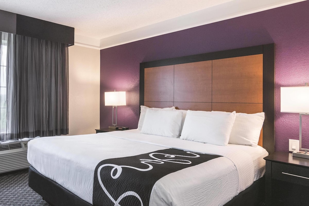 Ett hotellrum med en stor säng, en sänggavel och ett fönster med gardiner.