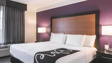 Une chambre d’hôtel avec un grand lit, une tête de lit et une fenêtre avec des rideaux.