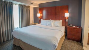 A hotel room with a large bed, two bedside tables with lamps, a wooden headboard, and a view of the outside through the curtains. - Residence Inn by Marriott Pensacola Downtown (Pensacola)