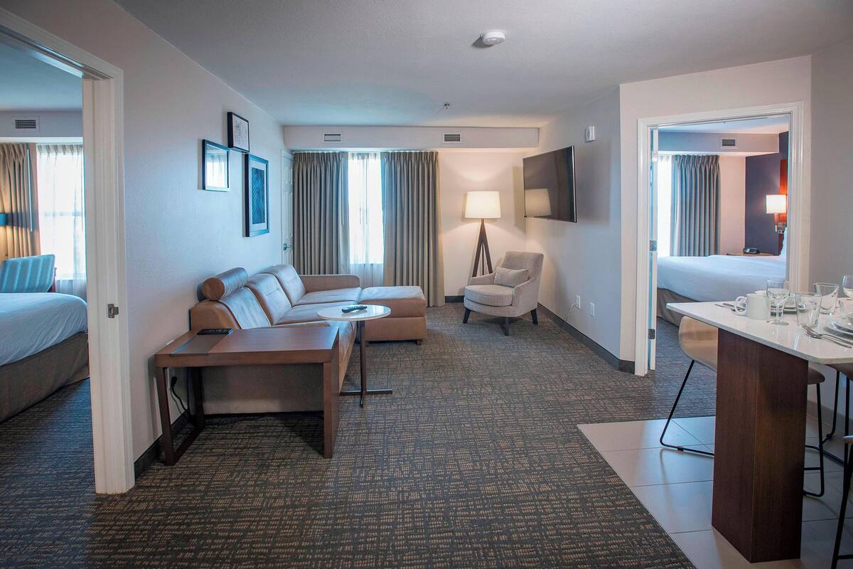 A hotel room with a bed, a sofa, a desk, a chair, and a TV.