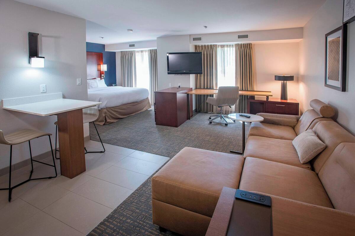 A hotel room with a bed, a desk with a computer, a sofa, and a TV.