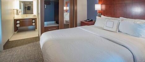 Habitación de hotel con una cama grande, cabecera de madera, baño con lavamanos y espejo, y vestidor.