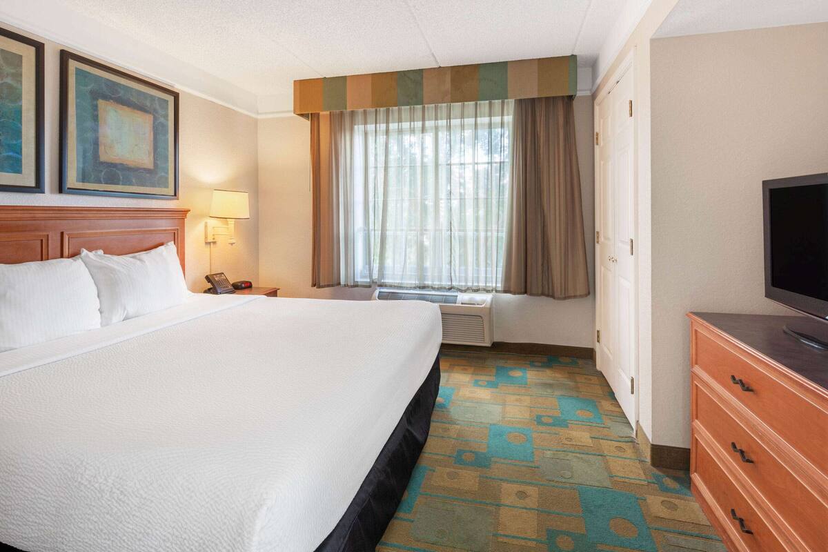 Habitación de hotel con una cama grande, un televisor de pantalla plana, un escritorio con lámpara y una ventana con cortinas.
