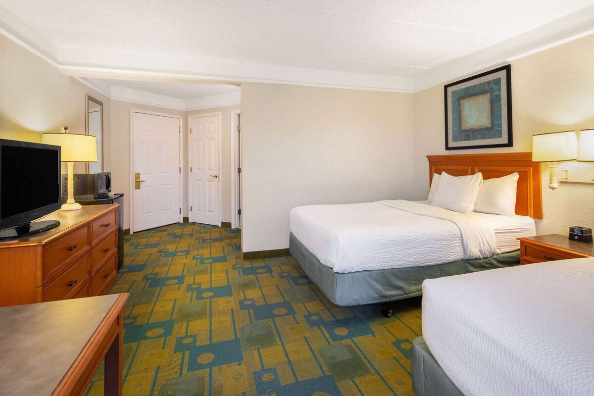 Una habitación de hotel con dos camas, televisión, escritorio y alfombra estampada.