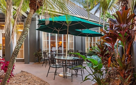 An indoor patio area with tables and chairs, surrounded by plants and umbrellas.
