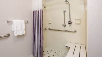 Une salle de bain équipée d’une douche, de barres d’appui, d’un porte-serviettes et d’une petite table avec des articles de toilette.