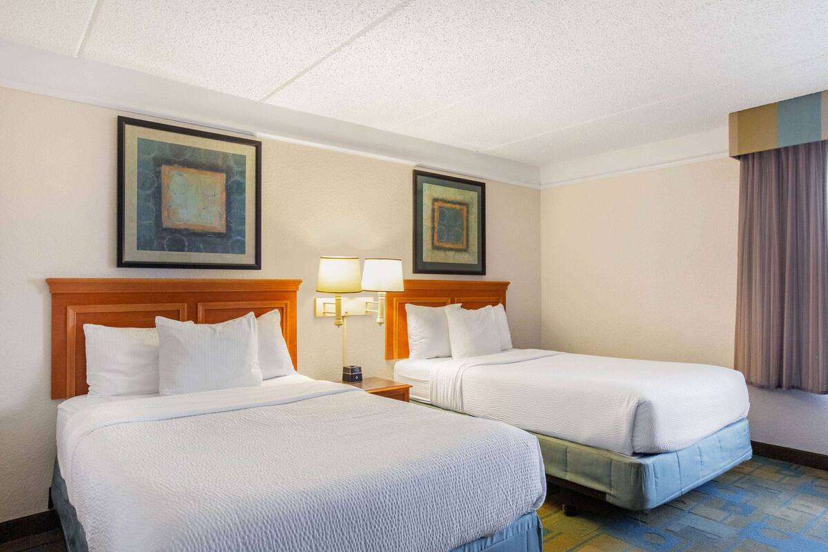 Una habitación de hotel con dos camas, una mesita de noche con una lámpara y dos obras de arte enmarcadas en la pared.