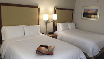A hotel room with two beds, each with white linens, a nightstand with a lamp, and a painting on the wall.